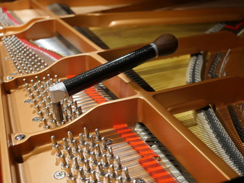 Piano tuning hammer resting on the tuning pins and strings of a grand piano